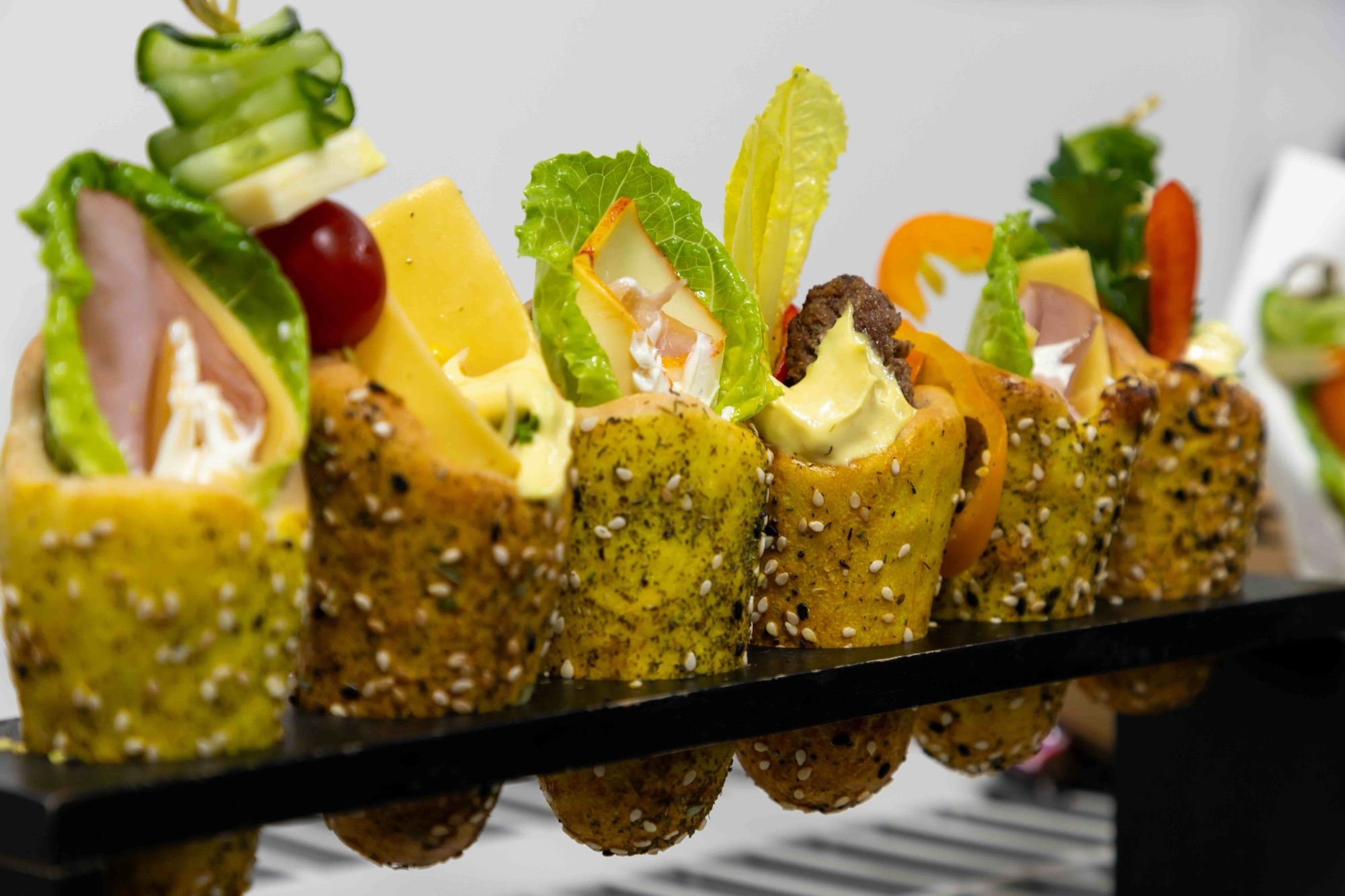 A row of sesame mini BreadKones with ham, cheese, and vegetable skewers on a black stand