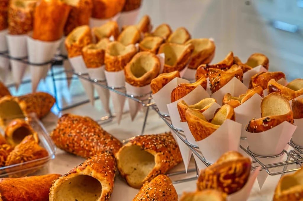 Empty BreadKones standing in paper cones on wire racks, with sesame-topped cones in front