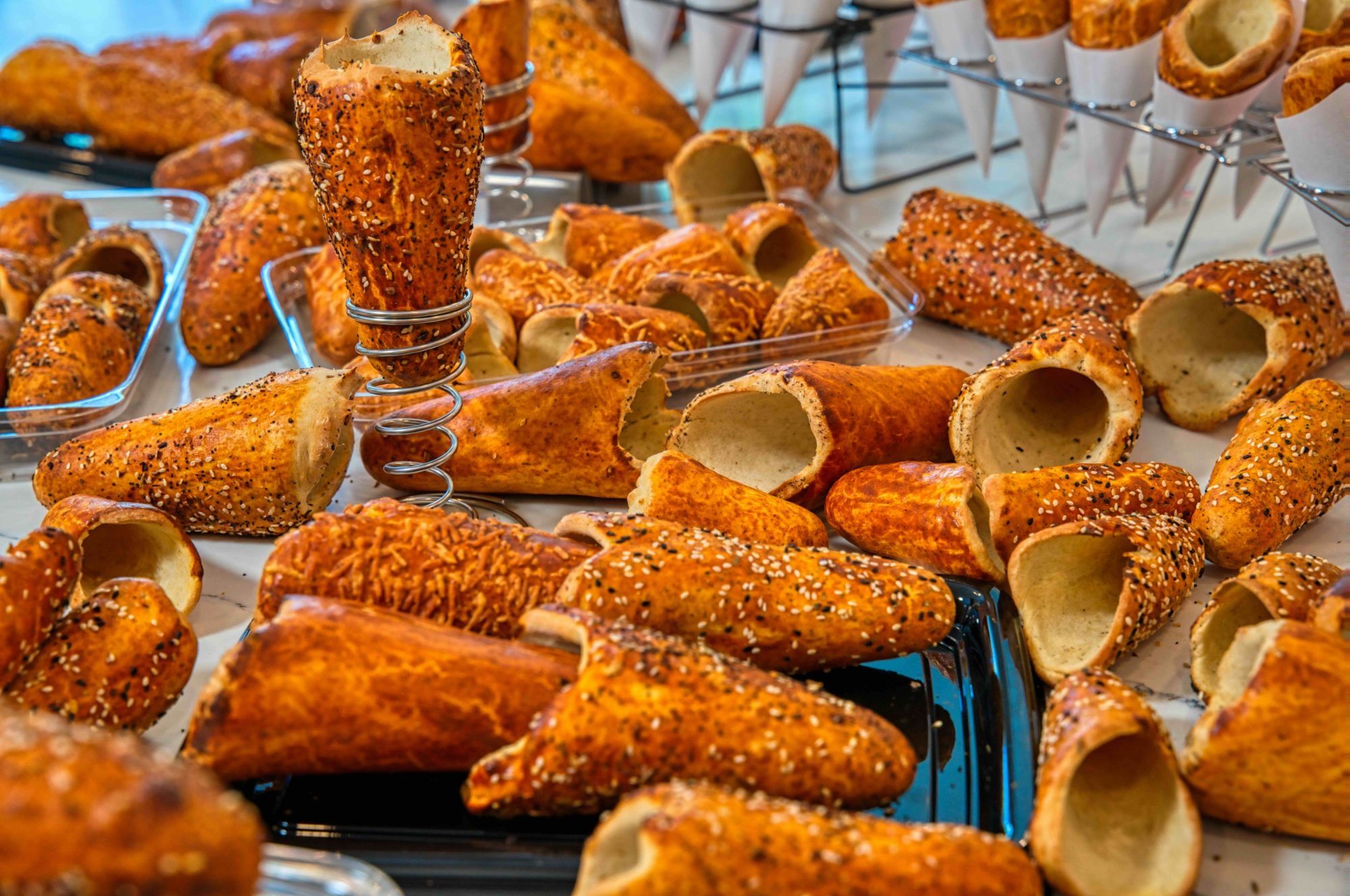 Empty BreadKones with sesame, everything, and cheese toppings across a display table, one standing in a wire holder