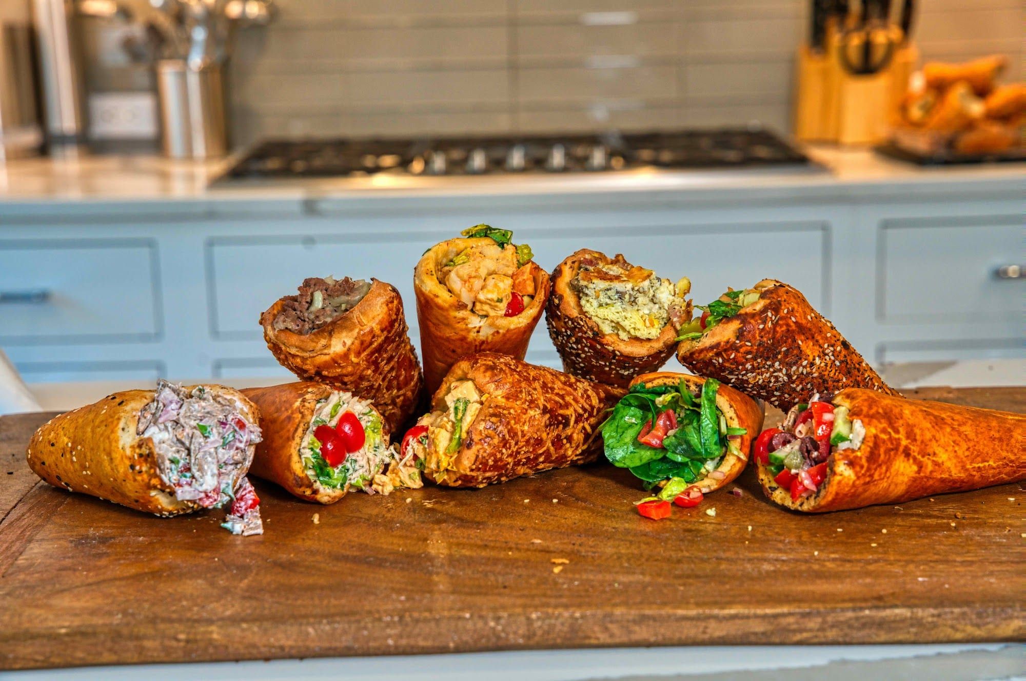 A row of BreadKones with assorted fillings on a wooden board in a kitchen