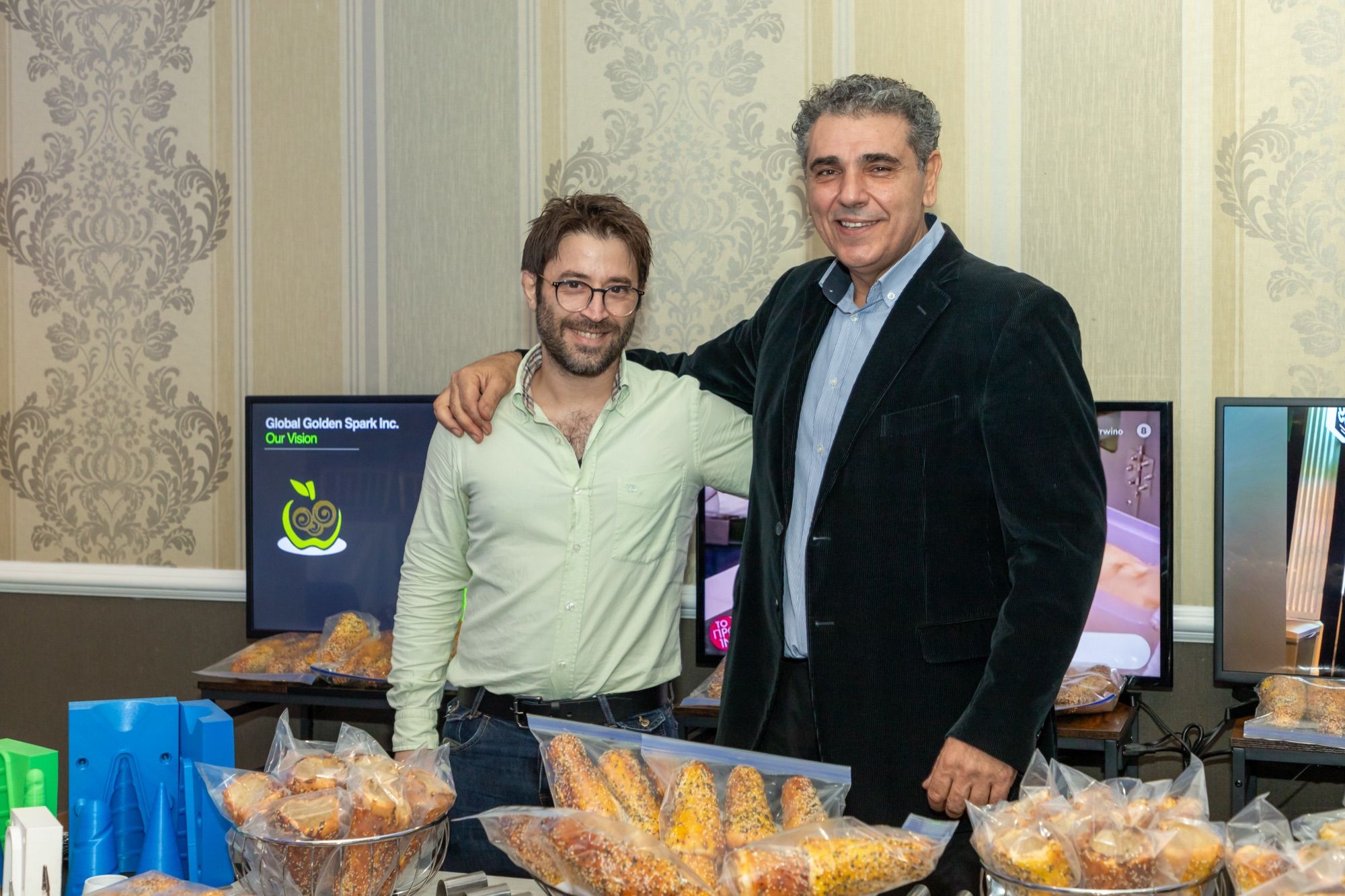 Two members of the BreadKone team at a Global Golden Spark presentation, behind a table of bagged BreadKones and cone molds