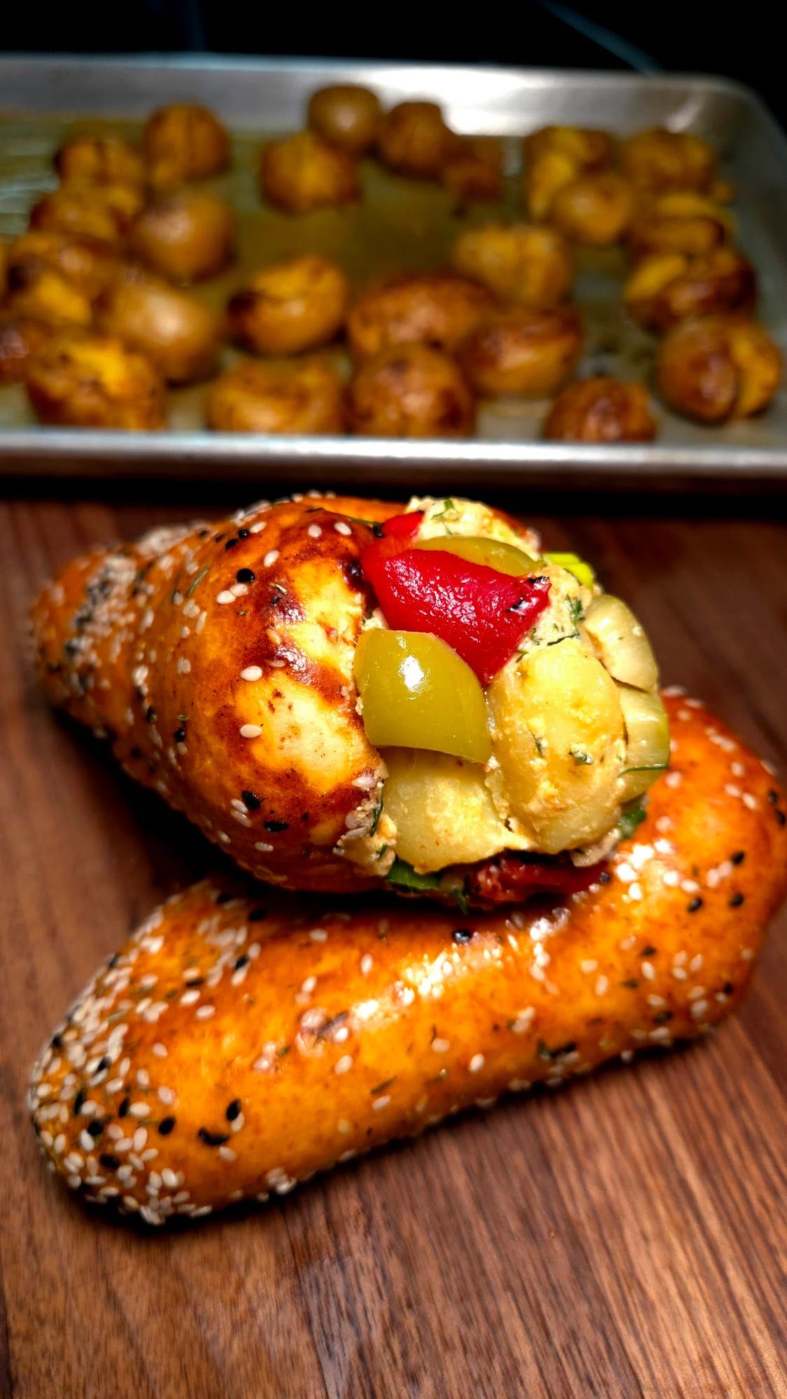 A sesame BreadKone stuffed with egg salad, roasted pepper, and olives, with a tray of more behind